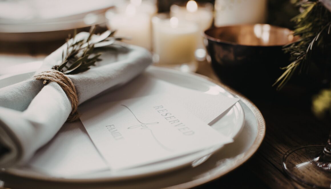 Soft-focus tabletop with linen napkin tied in twine over a place card, warm candlelight in the background.