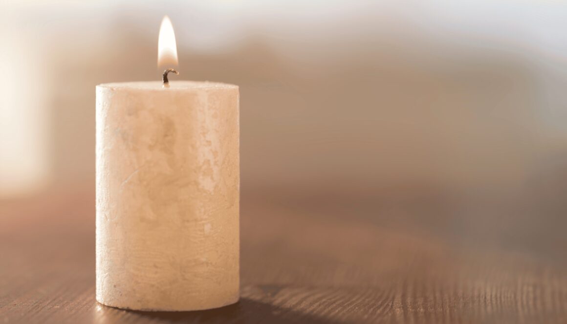 Ivory pillar candle burning on a wood surgace with a softly blurred neutral background.