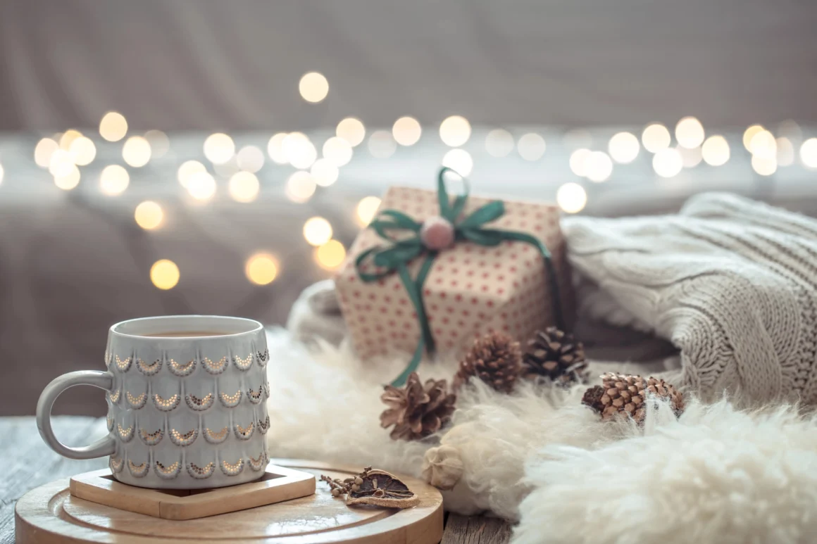 A serene winter scene featuring a ceramic mug, softly wrapped gifts, pinecones, and warm bokeh lights — evoking calm, tactile luxury, and the presence behind thoughtful giving.