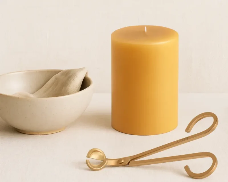 Minimalist tabletop with a neutral candle, ceramic bowl with lenen cloth, and brass wick trimmer — a small scene for evening light and example of a daily reset ritual.