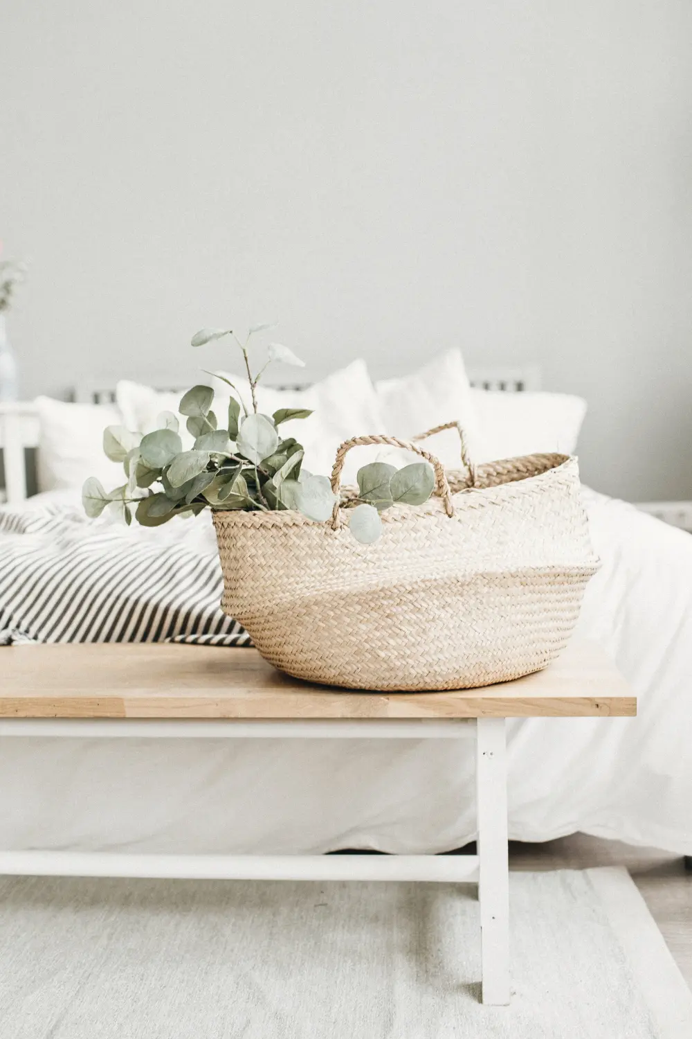 Woven basket with eucalyptus on a narrow bedroom bench, adding soft storage in the small space of a quiet luxury apartment.