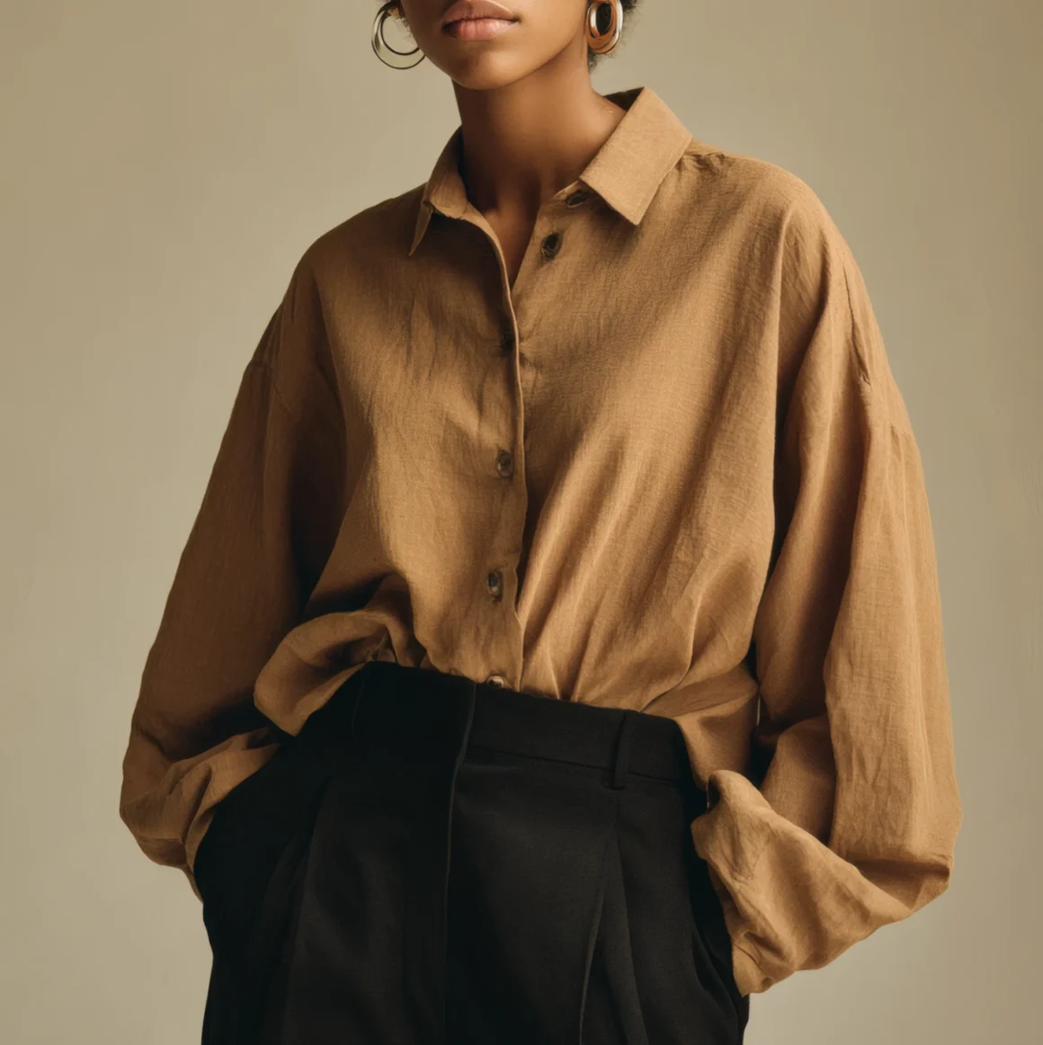 Woman wearing a soft brown shirt styled with tailored dark trousers, minimal jewelry, and natural texture defying a key quiet luxury myth.