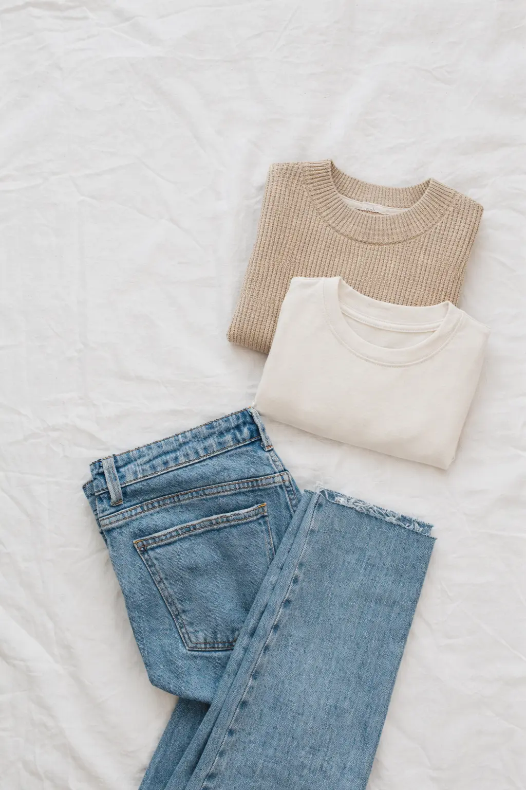 A quiet luxury outfit flat lay with jeans, an ivory tee, and a neutral knit ready to be layered.
