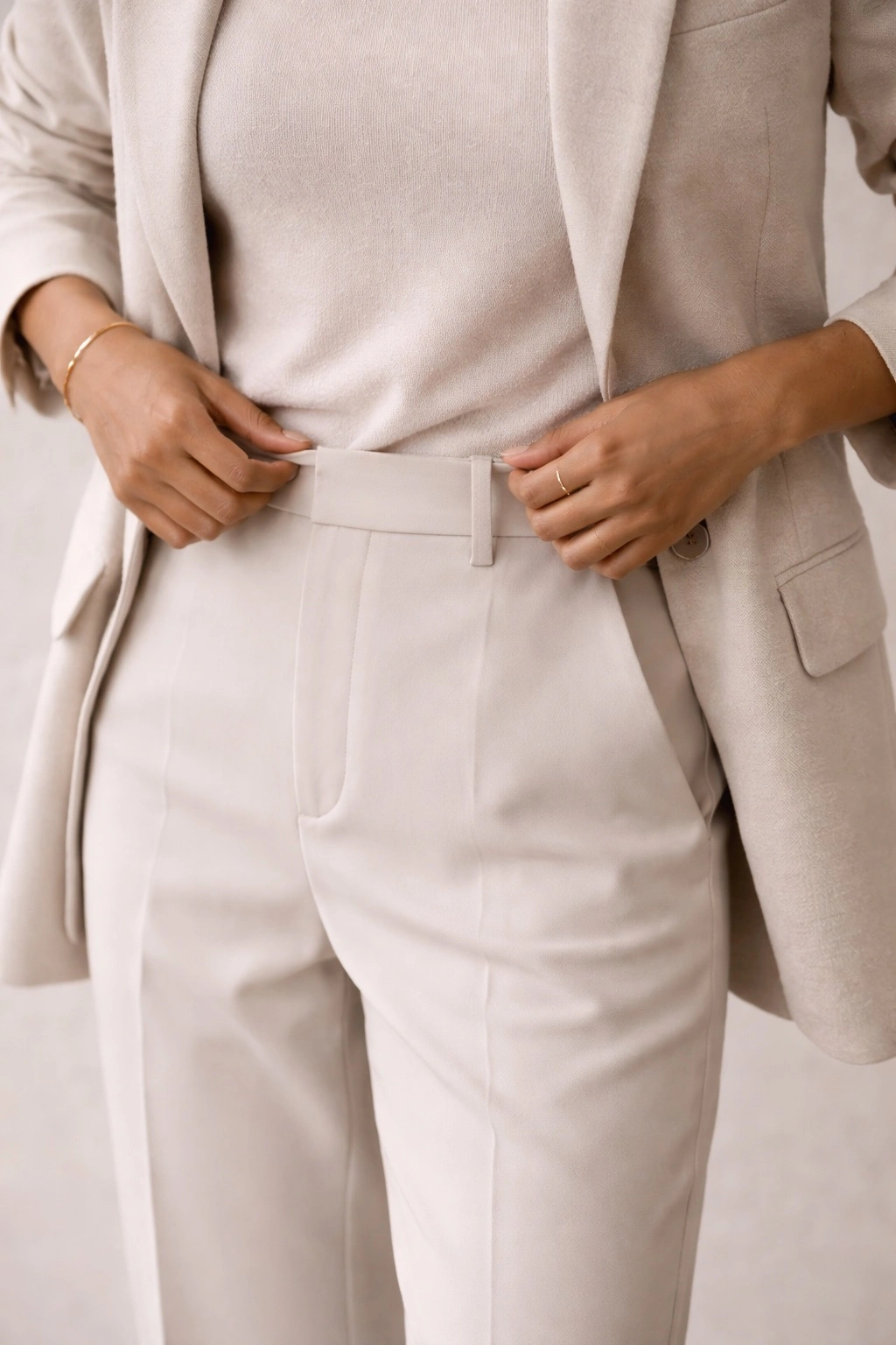 Hands adjusting the waistband on tailored trousers, illustrating subtle details in comfortable work outfits.